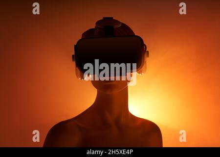 Femmina manichino con occhiali VR posizionati su sfondo arancione come simbolo della tecnologia futuristica Foto Stock