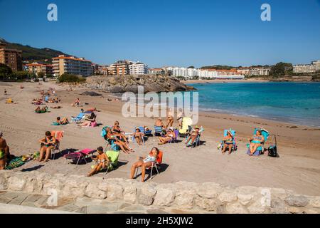Persone prendere il sole sulla spiaggia presso il porto marittimo spagnolo e località balneare di Castro Urdiales Cantabria sulla costa Cantabriana Spagna settentrionale Foto Stock