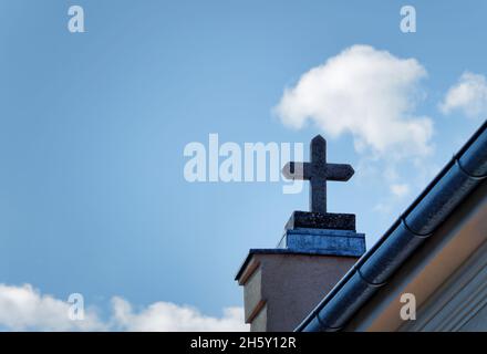 La croce di pietra in cima ad un edificio di chiesa contro un cielo blu nuvoloso durante il giorno Foto Stock