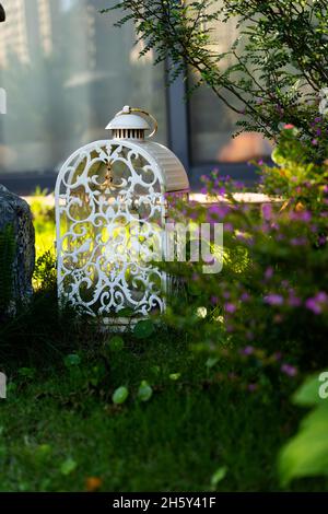 Un birdcage bianco d'annata in erba con fiori e cespugli Foto Stock