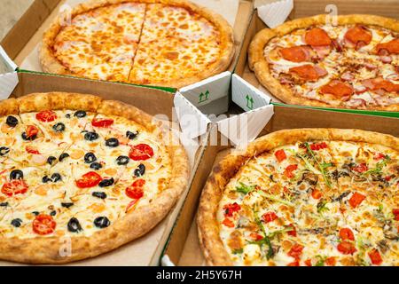Quattro diverse pizze tagliate sono in scatole quadrate. Carne e pizza vegetariana. Vista ravvicinata in prospettiva. Foto Stock