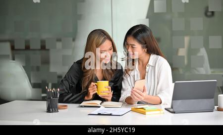 Le colleghe stavano facendo una conversazione interessante mentre mostravano alcuni contenuti sui loro smartphone. Foto Stock