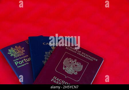 Tre diversi passaporti isolati su sfondo rosso. Passaporti canadesi, portoghesi e russi per l'ingresso in diversi paesi Foto Stock