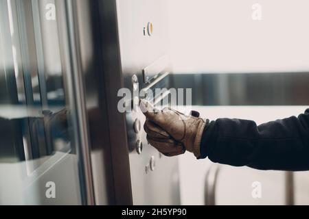 Primo piano del guanto di palma dell'indice premendo il pulsante elevatore durante la pandemia del virus del coronavirus covid-19 Foto Stock