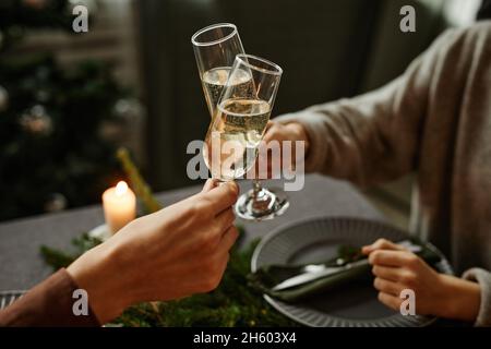 Primo piano di una giovane coppia che si gode la cena di Natale insieme e tostare con bicchieri di champagne mentre si siede accanto a un elegante tavolo da pranzo con candele Foto Stock