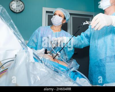 Una chirurgo femminile in uniforme chirurgica e una maschera protettiva esegue un intervento laparoscopico. Il medico osserva attentamente il monitor durante l'intervento chirurgico. Messa a fuoco selettiva. Foto Stock
