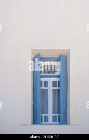 Finestra di legno blu contro pareti bianche di edifici tradizionali dell'isola greca Foto Stock