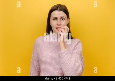 Ritratto di travagliato pensionato pensivo preoccupante paura sbagliato donna giovane mordente unghie dita guardare fotocamera, indossando maglia rosa maglione Foto Stock