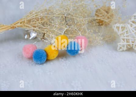 Orecchini a pompon colorati a forma di tre palle di furry.Orecchini sono accanto a prodotti di rattan, esemplari di fiori e altri ornamenti Foto Stock