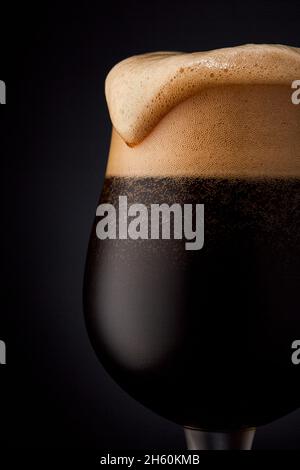 Primo piano di un bicchiere di birra scura su sfondo nero. Foto Stock