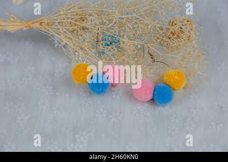 Orecchini a pompon colorati a forma di tre palle di furry.Orecchini sono accanto a prodotti di rattan, esemplari di fiori e altri ornamenti Foto Stock