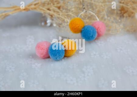 Orecchini a pompon colorati a forma di tre palle di furry.Orecchini sono accanto a prodotti di rattan, esemplari di fiori e altri ornamenti Foto Stock