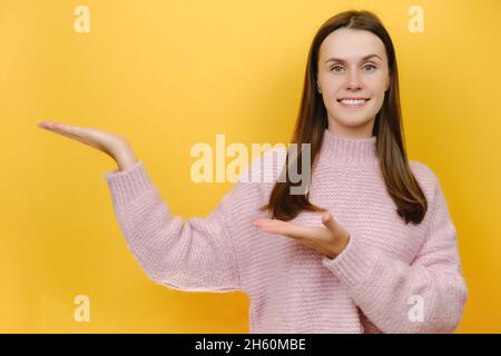 Sorridente felice bello millennial femmina indossare rosa maglia maglione indice di puntamento dito a parte area di lavoro copia spazio mockup Foto Stock