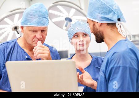 Il team di medici e il medico assistente discutono l'operazione sul computer portatile in chirurgia Foto Stock