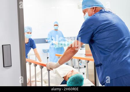 Due infermieri spingono il paziente nel letto dell'ospedale nella sala operatoria dell'intervento chirurgico Foto Stock