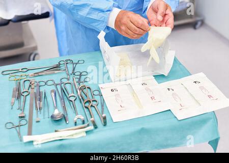 Il medico dispone gli strumenti chirurgici e indossa guanti monouso prima dell'intervento Foto Stock