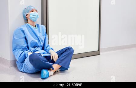 Infermiere o medico esausto seduto sul pavimento nel pronto soccorso della clinica Foto Stock