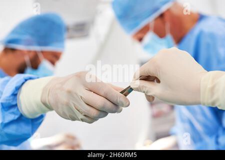 Il chirurgo assiste una procedura nel pronto soccorso e passa uno strumento chirurgico Foto Stock