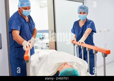 Due infermieri spingono il paziente con il falcetto per un intervento chirurgico nel corridoio ospedaliero Foto Stock