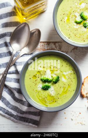 Ciotole di crema di broccoli con olio d'oliva, pepe e fette di pane tostate su un rustico tavolo di legno bianco Foto Stock