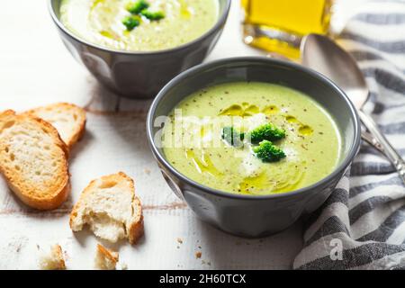 Ciotole di crema di broccoli con olio d'oliva, pepe e fette di pane tostate su un rustico tavolo di legno bianco Foto Stock