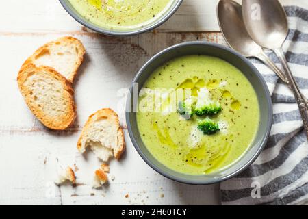 Ciotole di crema di broccoli con olio d'oliva, pepe e fette di pane tostate su un rustico tavolo di legno bianco Foto Stock