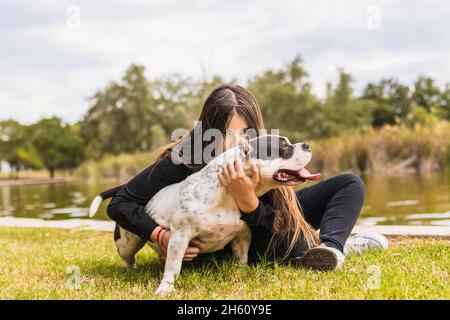 Giovane femmina che bacia un cane mentre si siede accanto ad un fiume Foto Stock