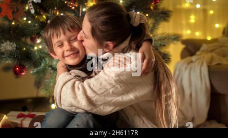 Ritratto di felice madre baciare il suo figlio sorridente in guancia mentre festeggia Natale o Capodanno