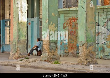 Scena stradale nel centro di l'Avana. Architettura coloniale sbriciolante con uomo seduto, la Habana (l'Avana), Habana, Cuba Foto Stock