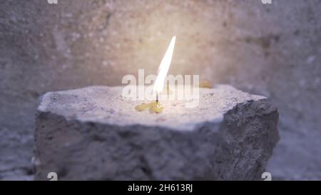 Primo piano di una candela che brucia in una vecchia chiesa. Riprese. Primo piano le bellissime candele bruciate su sfondo grigio scuro parete. Foto Stock