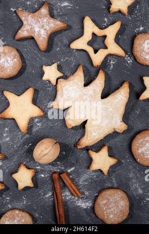 Biscotti natalizi fatti in casa di diverse forme, cannella, noci su sfondo nero da vicino. Natale cottura festiva per i bambini idea. Vista dall'alto, piatto. Foto Stock