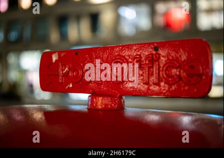 Un cartello sulla parte superiore di una tradizionale Red Post Box britannica che punta verso un ufficio postale Foto Stock