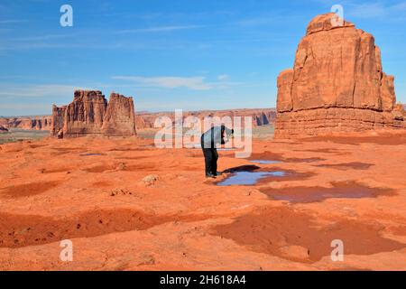 Visitatore che osserva i modelli di ghiaccio nelle pozze di roccia rossa, Arches National Park, Utah, USA Foto Stock