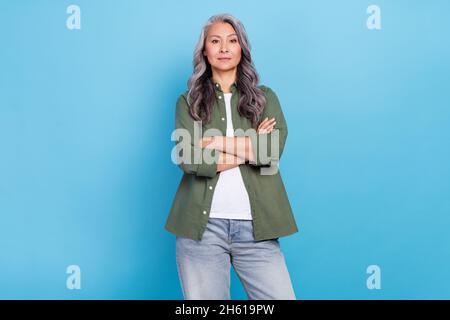 Foto di rigido anziano bianco hairdo signora braccia incrociate indossare khaki camicia jeans isolato su sfondo blu Foto Stock