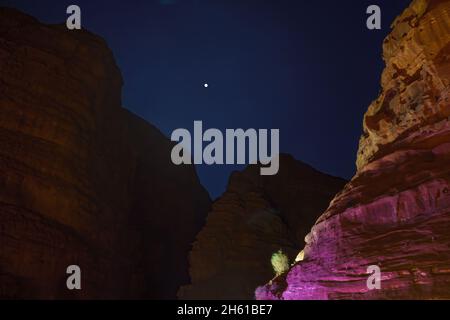 Vista notturna delle scogliere rocciose e della luna, a Wadi Rum, parco del deserto nel sud della Giordania Foto Stock