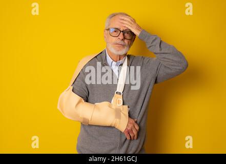 Uomo maturo con una stecca di braccio sorridente al segno della macchina fotografica isolato su sfondo giallo Foto Stock