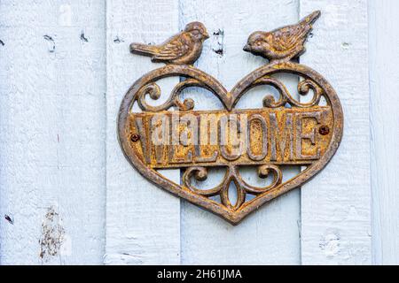 Targa di benvenuto in ghisa con cuore e due uccelli su una porta di legno Foto Stock