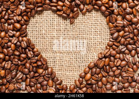Vista in formato completo di una struttura a forma di cuore in chicchi di caffè torrefatti su un tessuto in tela. Foto Stock
