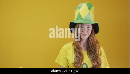 Sostenitore del Brasile. Donna rossa brasiliana festeggia il calcio, partita di calcio su sfondo giallo. Colori del Brasile. Indossare una t-shirt, una bandiera e una f Foto Stock