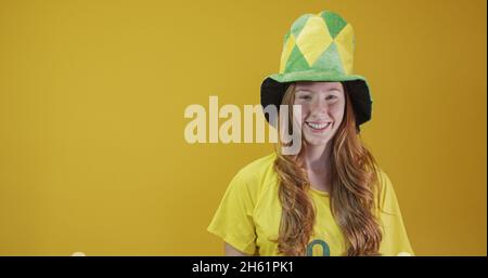 Sostenitore del Brasile. Donna rossa brasiliana festeggia il calcio, partita di calcio su sfondo giallo. Colori del Brasile. Indossare una t-shirt, una bandiera e una f Foto Stock