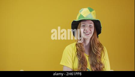 Sostenitore del Brasile. Donna rossa brasiliana festeggia il calcio, partita di calcio su sfondo giallo. Colori del Brasile. Indossare una t-shirt, una bandiera e una f Foto Stock