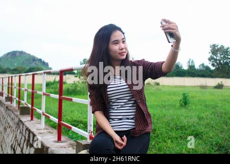 Una giovane bella donna vietnamita che prende selfie in giardino Foto Stock