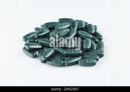 Compresse verdi con vitamine e spirulina per gli uomini su sfondo bianco. Multivitaminici per la salute degli uomini, isolare, spazio libero Foto Stock