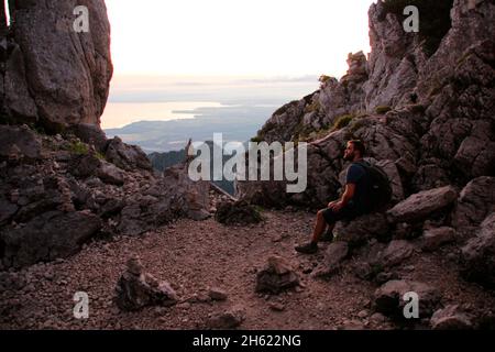 giovane uomo che si riposa, escursione fino alla cima del kampenwand (1669 m) nel chiemgau, alpi chiemgau, vicino aschau, alta baviera, baviera, germania meridionale, germania Foto Stock