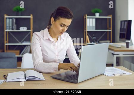 Giovane donna d'affari europea che lavora in ufficio su computer portatile con documenti elettronici. Foto Stock