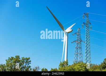 Turbina eolica bianca contro un cielo blu chiaro e torri ad alta tensione (linea elettrica) e spazio di riproduzione. Concetto di energia rinnovabile. Foto Stock