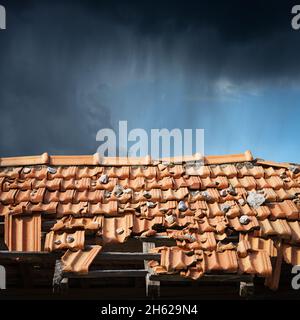 Primo piano di un tetto di una casa con pianelle in terracotta arancione (Pantiles, Coppo in italiano) danneggiate dall'uragano. Sullo sfondo un cielo piovoso scuro. Foto Stock