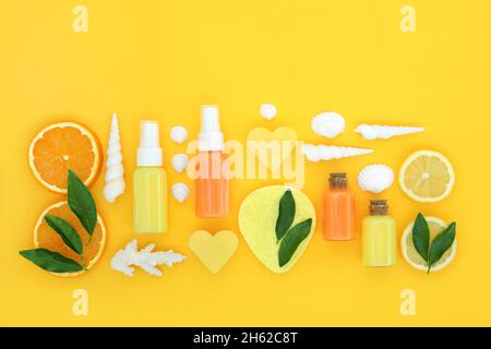 Rinfrescante trattamento di bellezza agli agrumi al limone e all'arancia per la cura della pelle. Idratante, lozione, sapone, spugna e conchiglie su sfondo giallo. Foto Stock