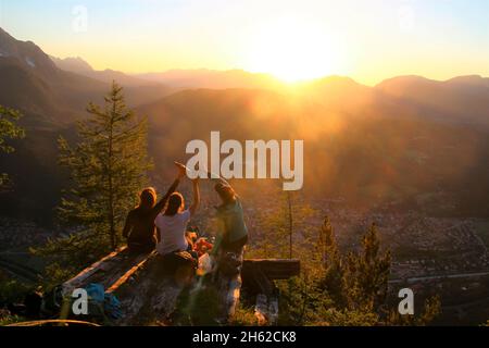 tre giovani donne celebrano, gioiscono in controluce, sullo sfondo il kranzberg, wettersteingebirge estergebirge al tramonto, fotografato al rifugio mittenwalder am karwendel, mittenwald, alta baviera, valle isar, baviera, germania, europa Foto Stock