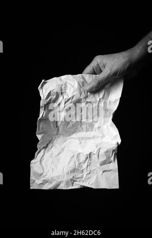 Immagine B+W di una mano maschio che tiene un foglio di carta sgualcito su sfondo nero con un'illuminazione straordinaria. Foto Stock